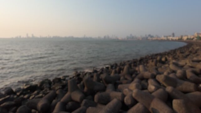 Bokeh view of beautiful sunset at Marine Drive, Mumbai, India. Blurred background footage of skyline at nariman point and arabian sea. Soft focus of coastal embankment with tetrapod structure.
