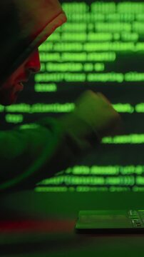 Hooded hacker in a dark room, celebrating a successful system hack with excitement by raising his fists and shouting yes. Cyber attack, data theft and cybersecurity threat. Vertical video