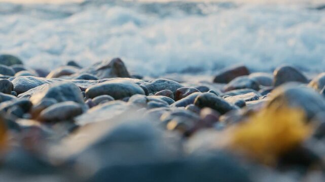 Soft ocean waves washing over smooth pebbles at golden sunset beach creating tranquil coastal atmosphere