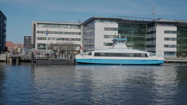 Modern passenger ferry docked at urban waterfront with contemporary office buildings and city infrastructure