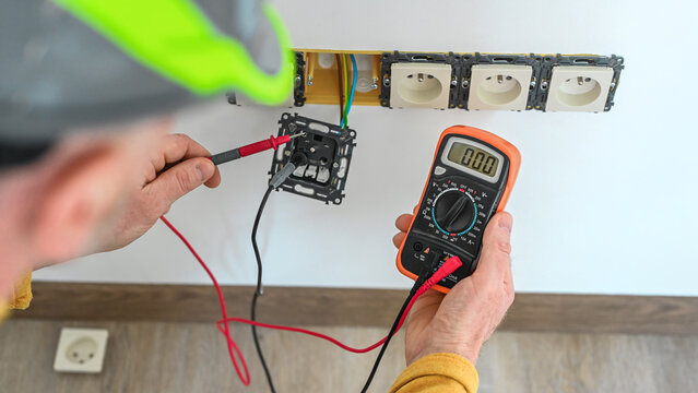 Electrical installation. The electrician's hands measure the voltage in an electrical outlet using a multimeter during installation a wall multi pack socket.