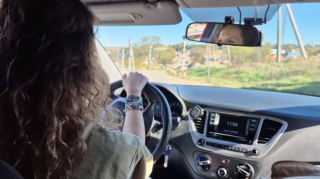 Driving road trip travel. Young woman maneuvering car through a sunny rural landscape on a pleasant day.