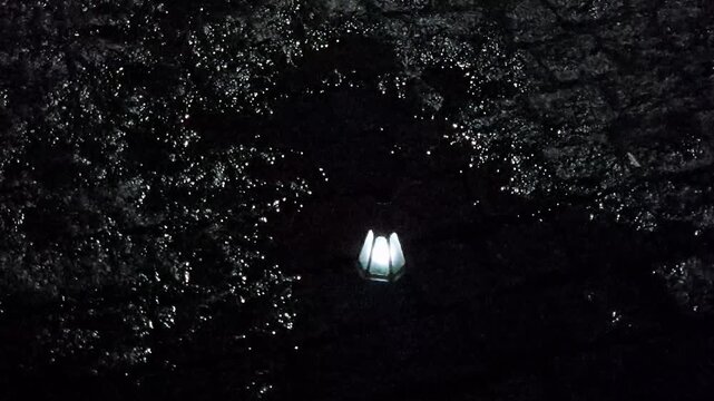 Water light night. A lone glowing object floats and spins in a shallow puddle on wet cobblestone pavement after heavy rain.