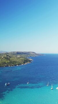 Scenic aerial view of the turquoise waters and lush coastline at Plage du Petit Sperone in Corsica, with boats anchored in the clear sea under a bright blue sky.