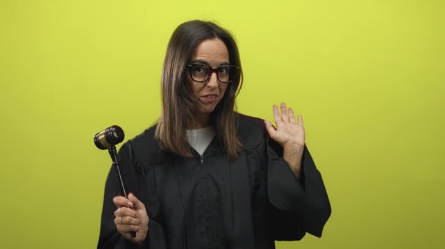 Woman judge in black robe holding wooden gavel and raising her hand in a bright green studio set, smiling with an expressive gesture; playful parody.