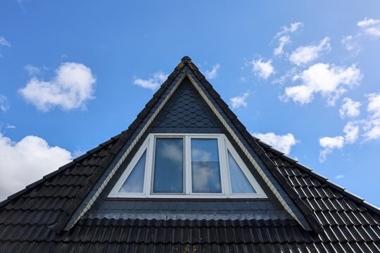 Building roof with dormer window against blue sky
