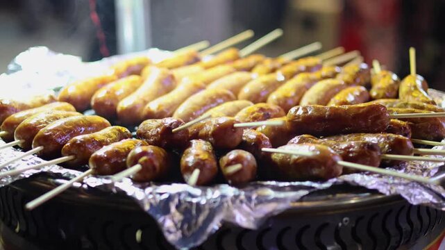 Close up on rows of delicious grilled sausages on skewers cooked over coals on a street food stall.