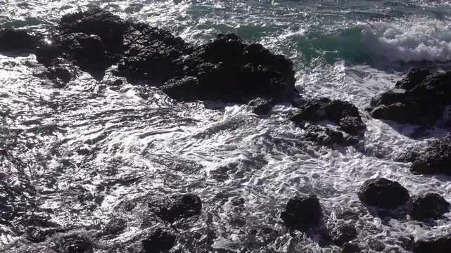 Waves breaking on rocks in bright sunlight, high contrast cinematic view