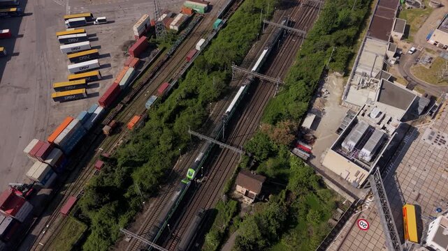 Train Yard Logistics: An aerial view reveals a bustling train yard filled with cargo containers, buses, and multiple trains on the tracks, showcasing industrial transportation and logistics.