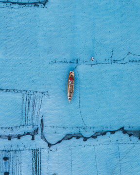 Aerial view of a weathered boat adrift on the aquamarine sea, the textures of the water contrasting with the boat's faded colors, Lembongan, Bali, Indonesia.