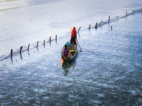 Aerial view of a boat gently glides through the shimmering waters, framed by rustic wooden posts and netting, Lembongan, Bali, Indonesia.
