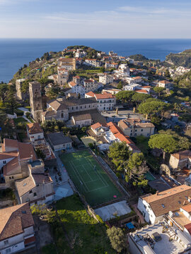 Aerial view of sun-drenched terracotta rooftops cascade down the hillside towards the azure sea, overlooked by the ancient tower in Ravello, Campania, Italy.