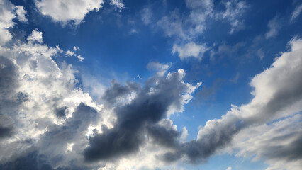 Obraz premium A partly cloudy sky, featuring white cumulus clouds alongside darker, denser clouds against a blue backdrop, displays a mix of white, fluffy clouds and darker, potentially rain-bearing clouds, typical