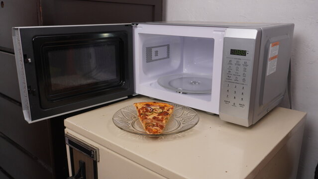 Concepto de almuerzo r&aacute;pido en el trabajo con rebanada de pizza y microondas en oficina moderna