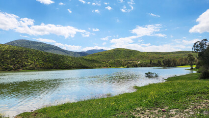 Fototapeta premium A scenic landscape featuring a calm lake surrounded by lush green hills and forests, reminiscent of natural areas found in Mediterranean climates