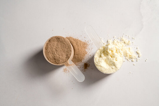 Vanilla and chocolate whey protein powder in scoops, food supplements, bright background