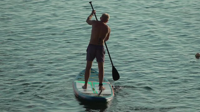 Paddleboarding man ocean. A fit male enjoying a peaceful summer day paddling on a stand up paddleboard in calm water.