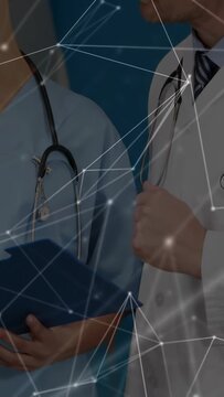 Vertical video: Reaching doctor in coat, nurse holding blue folder, reviewing in ward with overlay