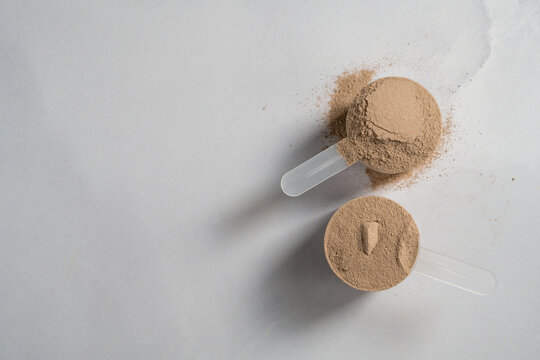 Chocolate whey protein powder in scoops, food supplements, dark background. Making protein shake drink.