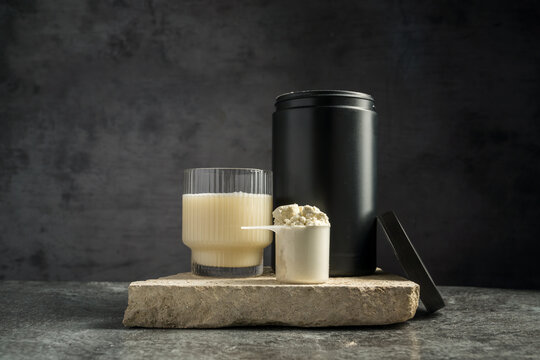 Protein shake in drinking glass and scoop with whey protein powder on dark background, copy space