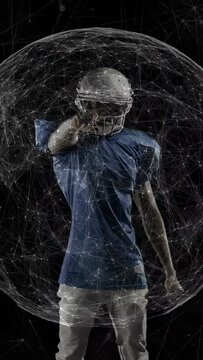 Posing football player in pads uncrossing arms, tapping helmet and pointing in studio with lit web