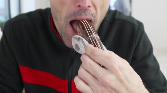 Eclair eating man Man sits in a cafe enjoying a delicious chocolate glazed eclair pastry with a joyful expression on his face