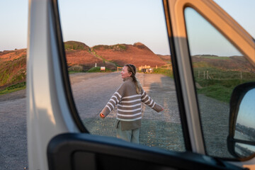 Naklejka premium Woman enjoying freedom on countryside road viewed through campervan window at sunset