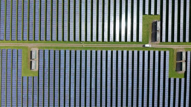 Aerial top down view of symmetrical solar panel rows on a sunny day in the UK countryside, renewable energy and sustainable power infrastructure.