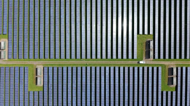Aerial top down view of symmetrical solar panel rows on a sunny day in the UK countryside, renewable energy and sustainable power infrastructure.