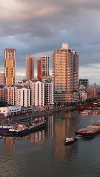 Modern high-rise buildings line the Pasig River as boats and barges navigate the water at sunset in Manila, Philippines.