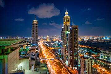 Panoramic night perspective of Dubai Downtown from rooftop showing high-rise buildings, Sheikh Zayed Road lights, and vibrant urban cityscape © jovannig