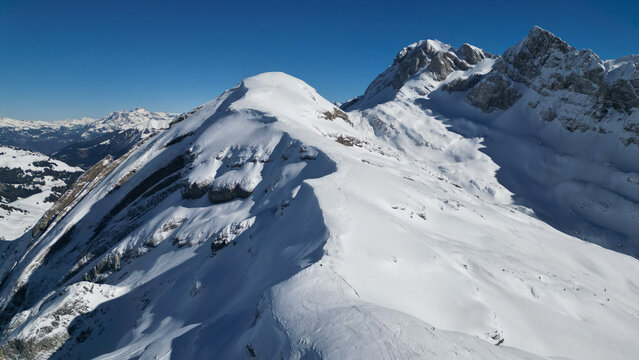 Aerial view of snow-dusted peaks under a crisp blue sky, revealing the rugged beauty of the French Alps, Samoens, Auvergne-Rhone-Alpes, France.