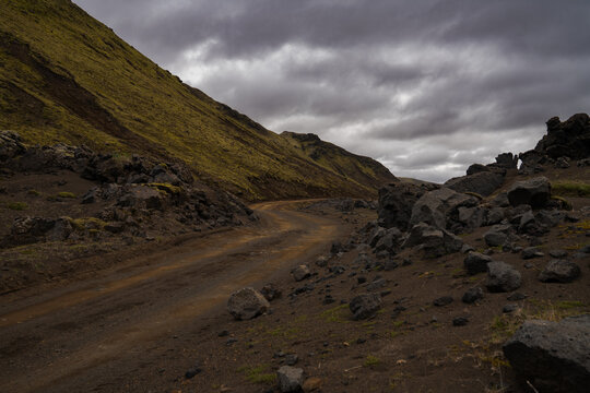 View of a winding dirt road cuts through the stark, rocky landscape under a heavy, moody sky, Skaftarhreppur, Skaftarhreppur, Iceland.
