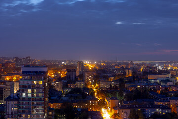 Obraz premium Dnipro, Ukraine, an expansive cityscape illuminated at twilight on May 18, 2023, showcasing a vibrant urban panorama with numerous illuminated buildings, bustling streets, and a prominent bridge spann