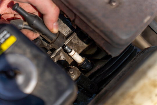 Close-up of hands attaching ignition wire to spark plug on gasoline engine of walk behind tractor, engine maintenance and setup outdoors.