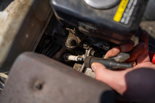 Close-up of hands attaching ignition wire to spark plug on gasoline engine of walk behind tractor, engine maintenance and setup outdoors.