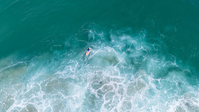 Aerial view of surfer paddling in turquoise ocean waves