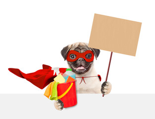 Naklejka premium Funny Pug puppy wearing superhero costume holds bucket with washing fluids and blank placard above blank white banner. Empty space for text. Isolated on white background