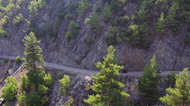 Aerial view of motorcyclists riding on a narrow rocky mountain road with sharp bends and steep cliffs. Adventure touring, remote travel, and rugged nature landscape captured in daylight.