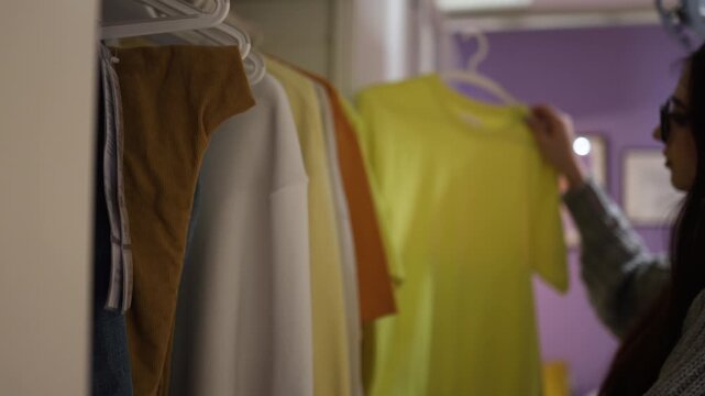 Young woman organizing wardrobe and choosing outfit at home fashion lifestyle minimal calm indoor dressing scene