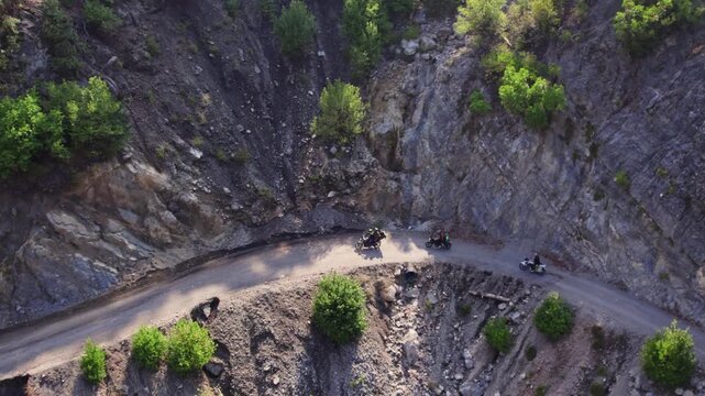 Aerial view of motorcyclists riding on a narrow rocky mountain road with sharp bends and steep cliffs. Adventure touring, remote travel, and rugged nature landscape captured in daylight.