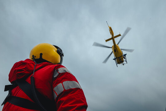Rear view of paramedic in red uniform and helmet watching air ambulance helicopter taking off. Themes rescue, help and hope.