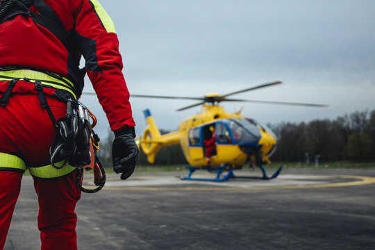 Paramedic running to helicopter of emergency medical service on helipad. Rescuer with safety harness and climbing equipment against helicopter. Themes rescue, help and hope.