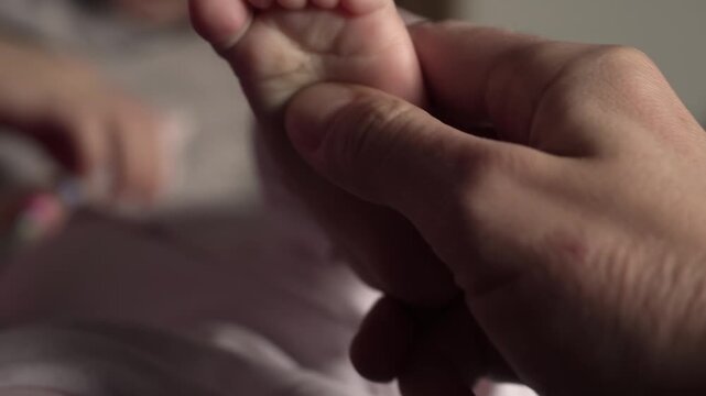 Dad massages the delicate skin on a small heel, baby's fingers, while mom plays with him on the bed