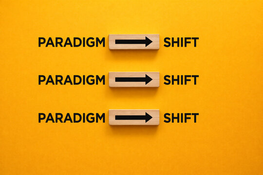 Wooden blocks featuring black arrows pointing right are arranged between the words paradigm and shift against a bright yellow background to illustrate a major conceptual.