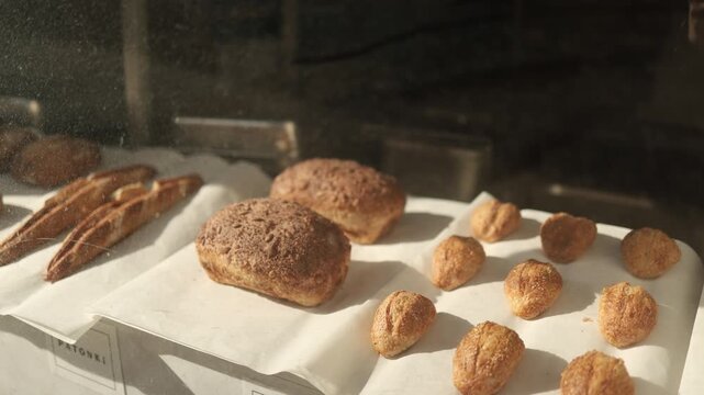 Assorted bread and sweet buns in bakery showcase behind glass window fresh baked products display retail food concept pastry shop interior warm atmosphere