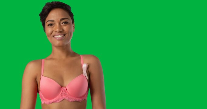 African american woman wearing a pink bra and ribbon badge smiling against black background