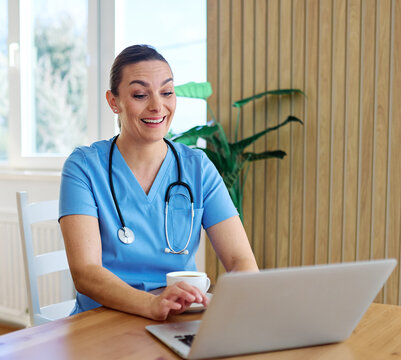 Portrait of a young nurse getting ready for work and using laptop online meeting at home. Overworked, busy, stress, urgency, multitasking concepts