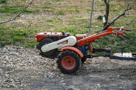 Orange and White Two wheel Tractor with a Trailer Parked on a Gravel Path