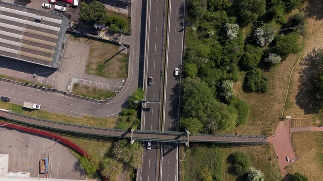Aerial View of Highway and Park: An aerial perspective reveals a bustling highway passing under a pedestrian bridge, adjacent to a vibrant green park and industrial building.